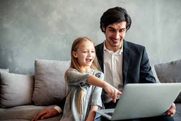 Glückliches kleines Mädchen, das mit ihrem Vater einen Film auf dem Computer sieht