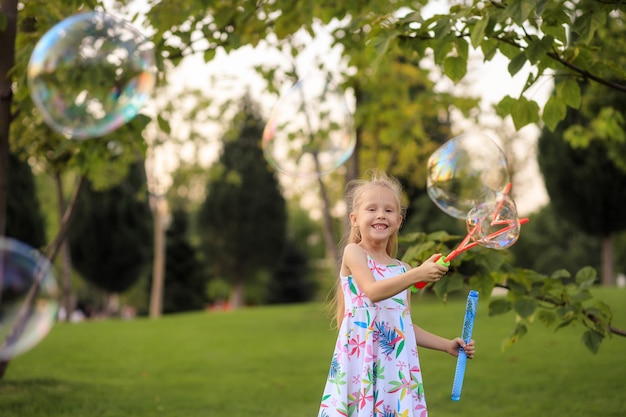 Glückliches kleines Mädchen, das mit Sommerseifenblasen im Park spielt.