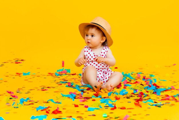 Glückliches kleines Mädchen in einem Kleid in Erbsen und in einem Strohhut fängt Konfetti auf gelbem Hintergrund. Platz für Text