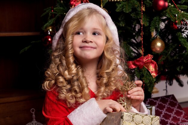 Glückliches kleines Mädchen in einem Kleid mit ihrem Weihnachtsgeschenk