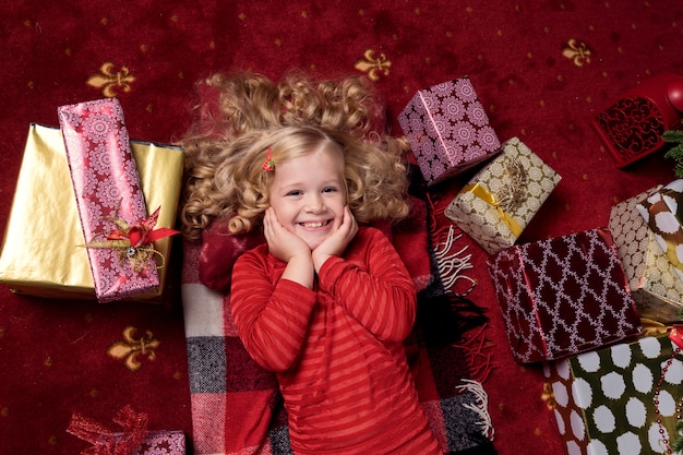 Glückliches kleines Mädchen in einem Kleid mit ihren Weihnachtsgeschenken