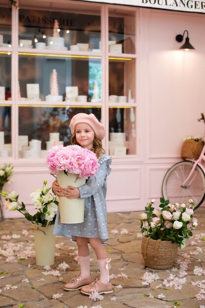 Glückliches kleines Mädchen in einem Kleid und in einer Baskenmütze mit einem Strauß rosa Pfingstrosen zum Muttertag