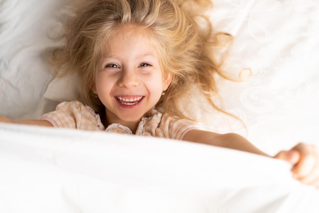 Glückliches kleines mädchen in einem weißen bett auf einem kissen guten morgen gesundes babyschlafkonzept