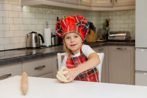 Glückliches kleines Mädchen kocht Weihnachtsplätzchen zu Hause in der Küche in einem Kochkostüm. kleine Blondine bereitet Kekse für das neue Jahr vor. festliches Frühstück, Mittagessen, Abendessen. Platz für Text. Foto in hoher Qualität