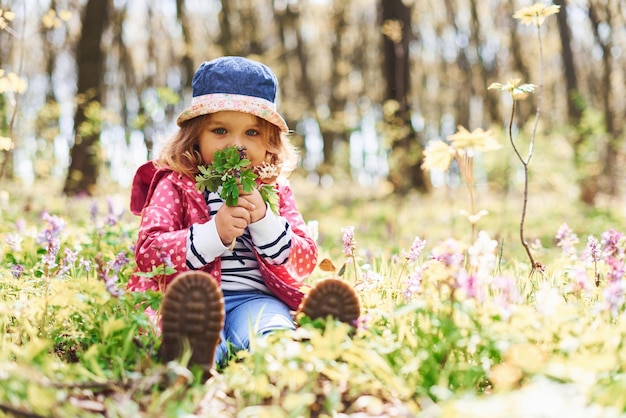 Glückliches kleines Mädchen mit blauem Hut hat tagsüber einen Spaziergang im Frühlingswald