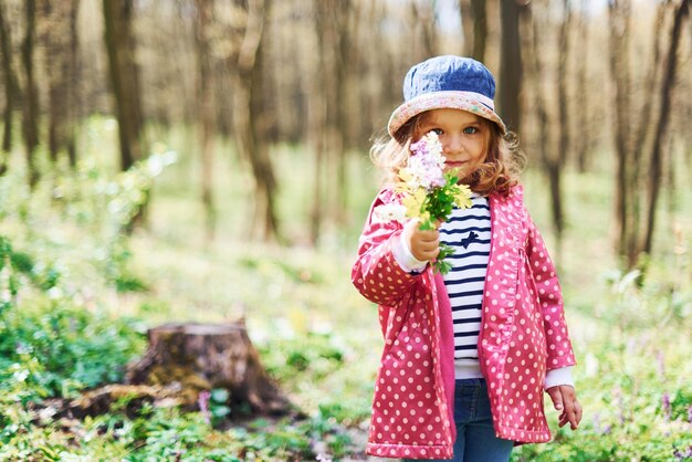 Glückliches kleines Mädchen mit blauem Hut hat tagsüber einen Spaziergang im Frühlingswald