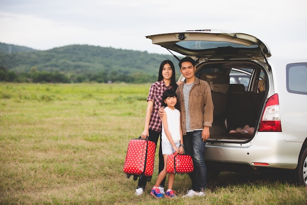 Glückliches kleines Mädchen mit der asiatischen Familie, die im Auto sitzt