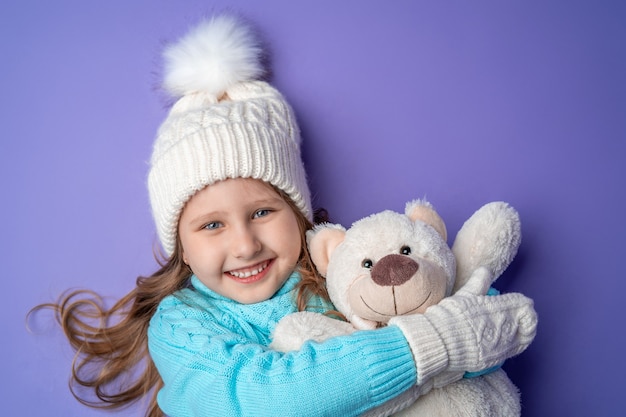 Glückliches kleines Mädchen mit Handschuhen, die einen Teddybär halten