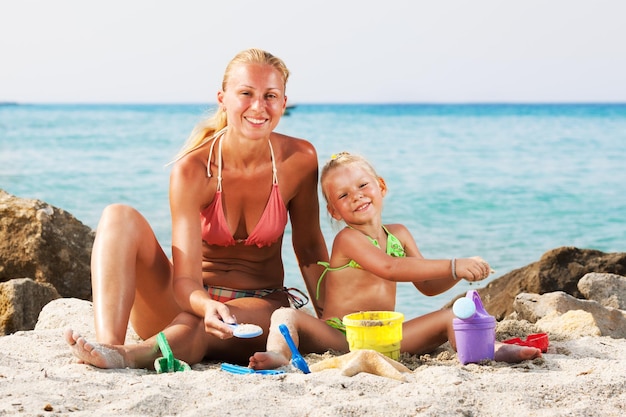 Glückliches kleines Mädchen mit Mutter am Strand mit Eimer und Spaten