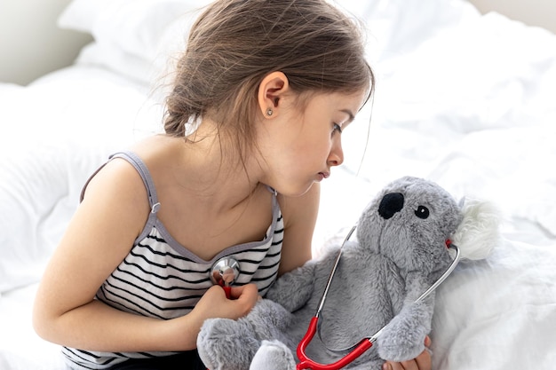 Glückliches kleines Mädchen mit Stofftierkoala im Bett