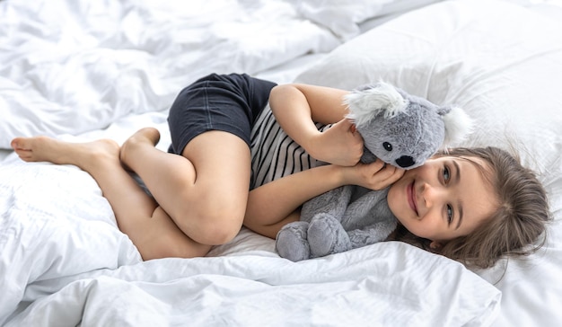 Glückliches kleines Mädchen mit Stofftierkoala im Bett