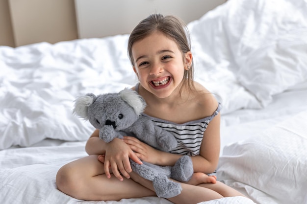 Glückliches kleines Mädchen mit Stofftierkoala im Bett