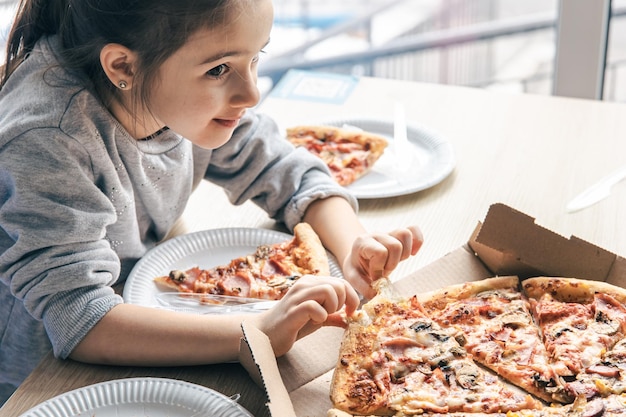 Glückliches kleines Mädchen schaut Pizza mit Appetit an