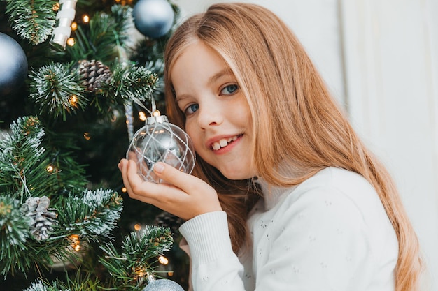 Glückliches kleines Mädchen schmücken Weihnachtsbaum zu Hause. Winterurlaub und Menschenkonzept