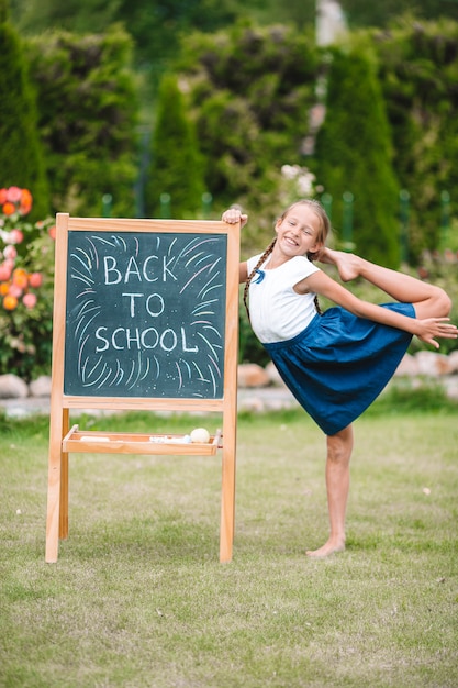 Glückliches kleines Schulmädchen mit einer Tafel im Freien