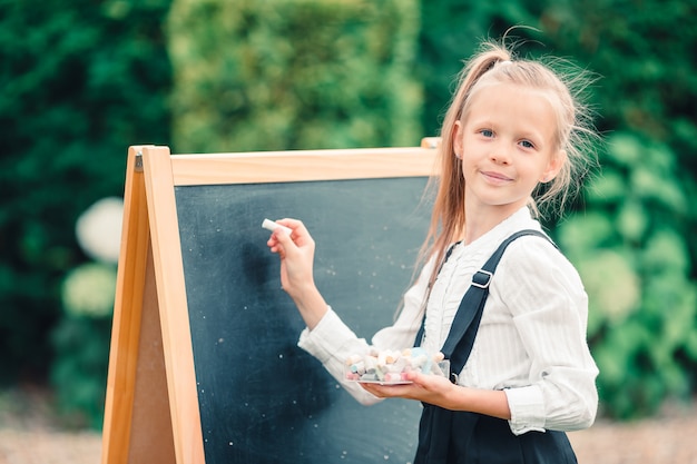 Glückliches kleines Schulmädchen mit einer Tafel im Freien