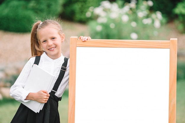 Glückliches kleines Schulmädchen mit einer Tafel im Freien