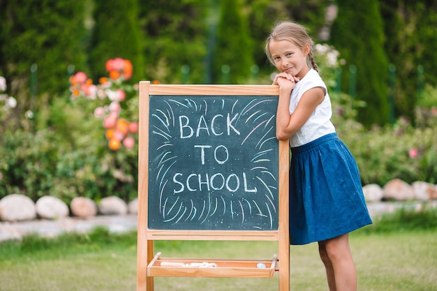 Glückliches kleines Schulmädchen mit einer Tafel im Freien