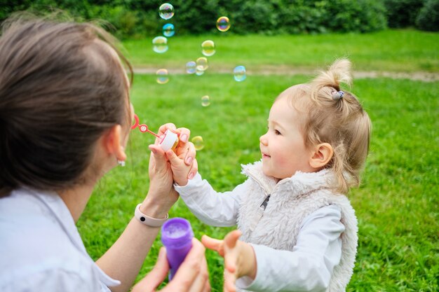 Glückliches Kleinkind und Mutter machen Seifenblasen in einem Sommerpark