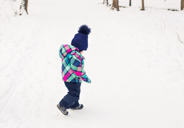 Glückliches Kleinkindmädchen, das am Weihnachtstag in einem schönen verschneiten Winterpark spielt.