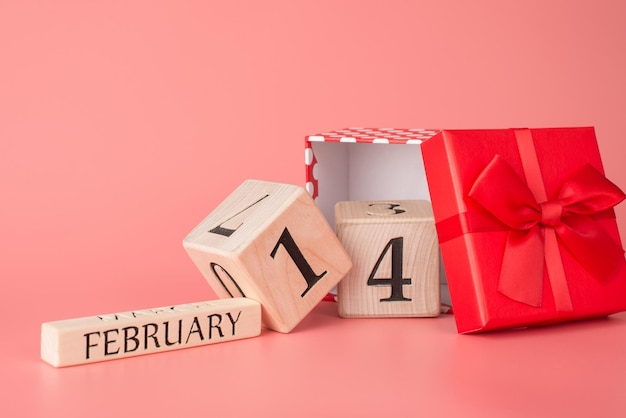 Glückliches kommendes Konzept vom 14. Februar. Foto von Holzklötzen, die aus einer offenen roten Geschenkbox fallen, isolierte helle Kulisse