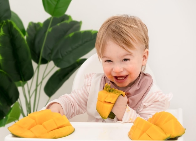 Glückliches lachendes kaukasisches Babymädcheninfanttoddlerkind isst Obst MangoKid hat Mahlzeitgesunde Nahrung