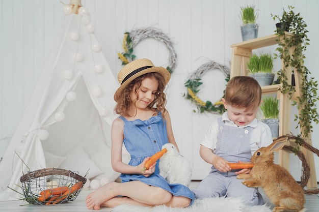 Glückliches lachendes kleines Mädchen und Junge, die mit einem Babykaninchen spielen