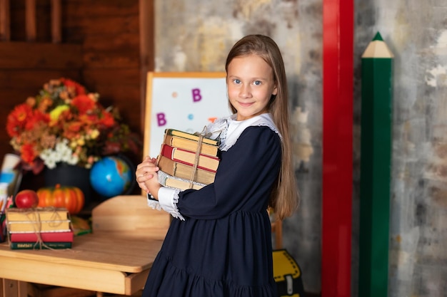 Glückliches Lächeln Kleines Mädchen mit Büchern steht in der Nähe der Tafel