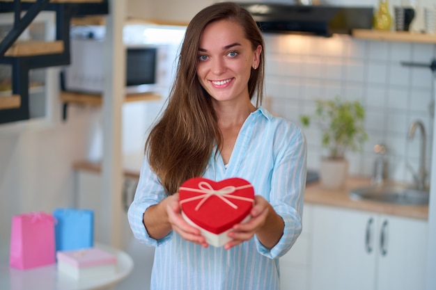 Glückliches Lächeln zufrieden niedliche geliebte Frau hält eine herzförmige Geschenkbox für Valentinstag für 14. Februar