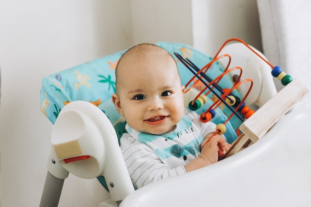 Glückliches lächelndes Baby, das zu Hause Spielzeug in einem Hochstuhl spielt