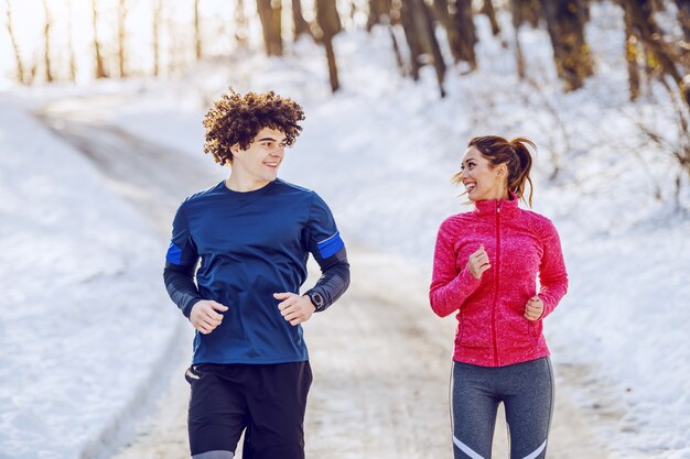 Glückliches lächelndes kaukasisches Paar in der Sportbekleidung, die in der Natur läuft, während sie einander betrachten. Winterzeit.