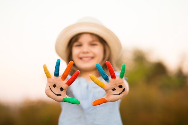 Glückliches lächelndes kleines Mädchen mit den Händen in der Farbe spielen im Freien im Sommerpark