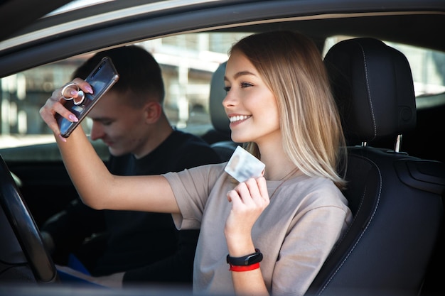 Glückliches lächelndes Mädchen macht ein Selfie mit einem neuen Führerschein und sitzt neben einem Lehrer.