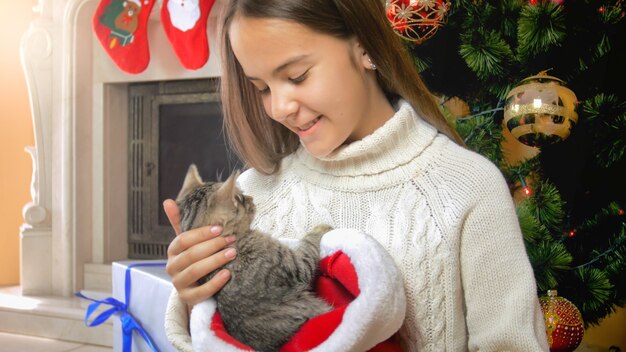 Glückliches lächelndes Mädchen mit Katze am Kamin und am Weihnachtsbaum