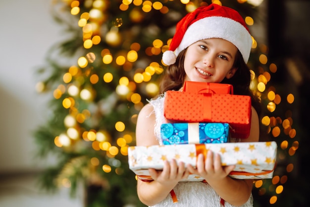 Glückliches lächelndes Mädchen mit Weihnachtsgeschenkboxen Nettes Kind hat Spaß in der Nähe von Baum