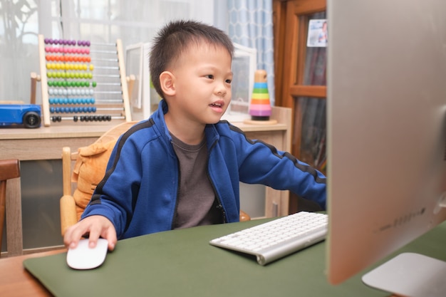 Glückliches lächelndes niedliches kleines asiatisches Kind mit Personalcomputer, der zu Hause Videoanruf macht, Kindergartenjunge, der online studiert und Schule über E-Learning besucht