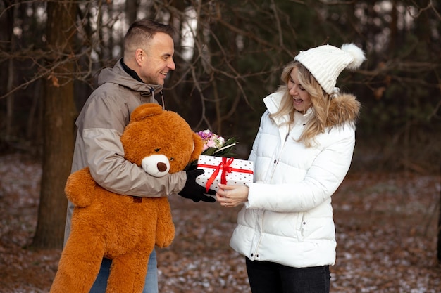 Glückliches lächelndes Paar tauscht Valentinstagsgeschenke im Winterwald während eines romantischen Dates aus. Liebeserklärung. Urlaub der Liebenden. Zärtlichkeit und Berührung. Liebe Emotionen. Lebensstile.