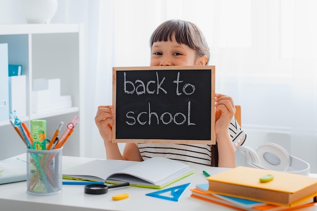 Glückliches lächelndes Schulkind, das eine kleine Tafel mit Text zurück zur Schule hält