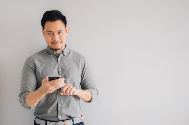 Glückliches Lächelngesicht des hübschen asiatischen Manngebrauchs-Smartphonestands lokalisiert auf grauem Hintergrund.