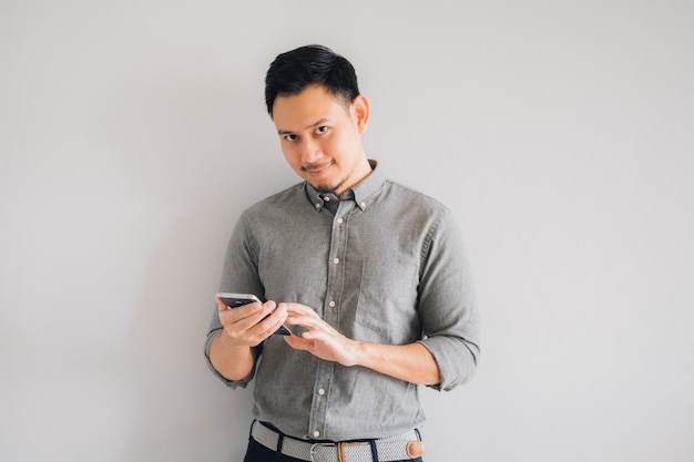 Glückliches Lächelngesicht des hübschen asiatischen Manngebrauchs-Smartphonestands lokalisiert auf grauem Hintergrund