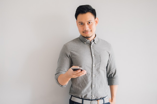 Glückliches Lächelngesicht des hübschen asiatischen Manngebrauchs-Smartphonestands lokalisiert auf grauem Hintergrund