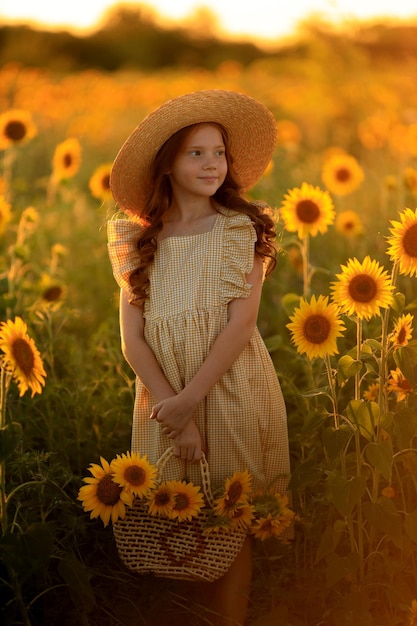 Glückliches Leben im Sommer Porträt eines schönen rothaarigen Mädchens mit Hut auf einem Sonnenblumenfeld mit Blumen in den Händen in den Strahlen der untergehenden Sonne