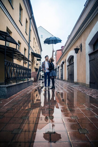 Glückliches Liebespaar, das sich an einem regnerischen Tag unter einem Regenschirm auf einer Stadtstraße küsst