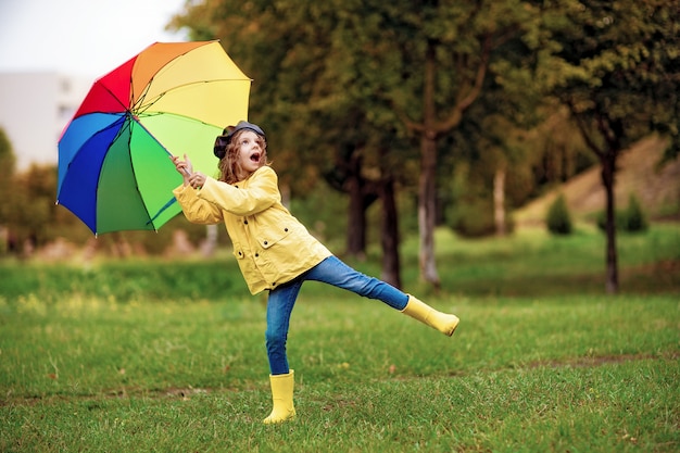 Glückliches lustiges Kindermädchen mit Regenschirm in den Gummistiefeln