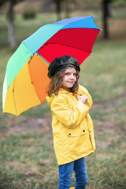 Glückliches lustiges Kindermädchen mit Regenschirm in den Gummistiefeln