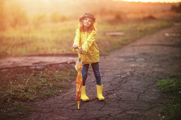 Glückliches lustiges Kindermädchen mit Regenschirm in Gummistiefeln