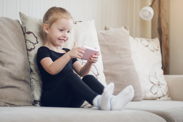 Glückliches lustiges Mädchen spielen auf Smartphone. Kinder beobachten Online-Cartoons, Kinder Computerabhängigkeit, Kindersicherung. Fernunterricht, Online-Unterricht für Kinder.