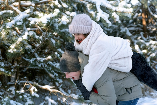 Glückliches Mädchen auf der Rückseite eines Kerls. Liebhaber, die Spaß im Winterwald haben.