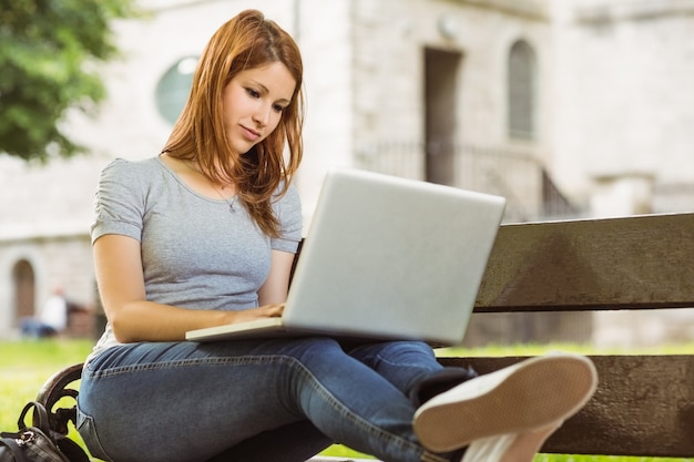 Glückliches Mädchen, das auf Bank unter Verwendung des Laptops sitzt