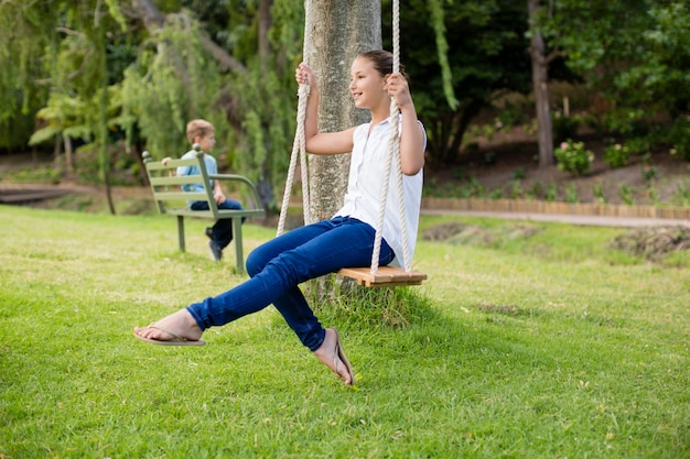 Glückliches Mädchen, das auf einer Schaukel im Park sitzt